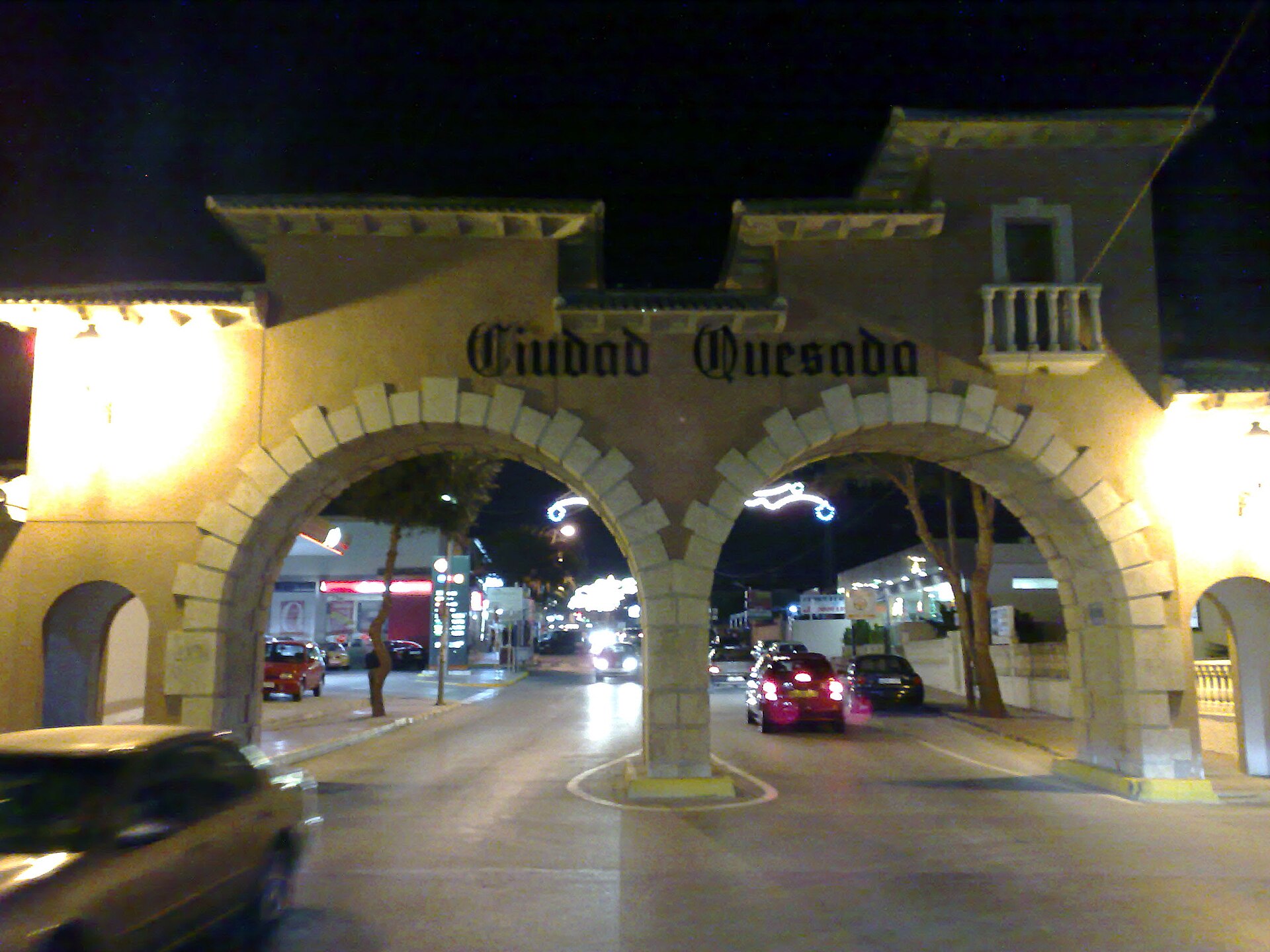 Arco de acceso nocturno con rótulo 'Ciudad Quesada'
