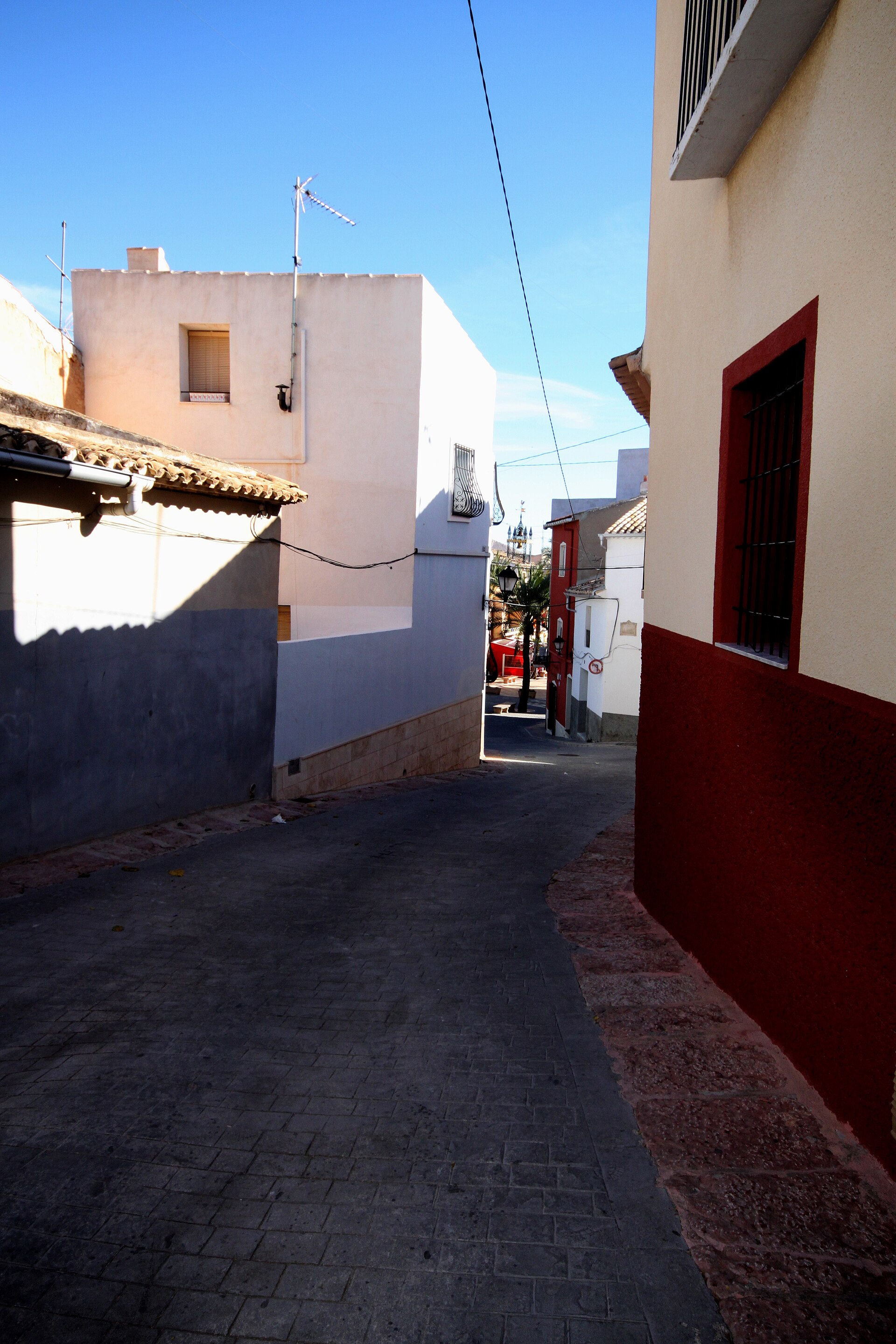 Calle estrecha en Hondón de las Nieves con fachadas y vista parcial de la plaza al fondo