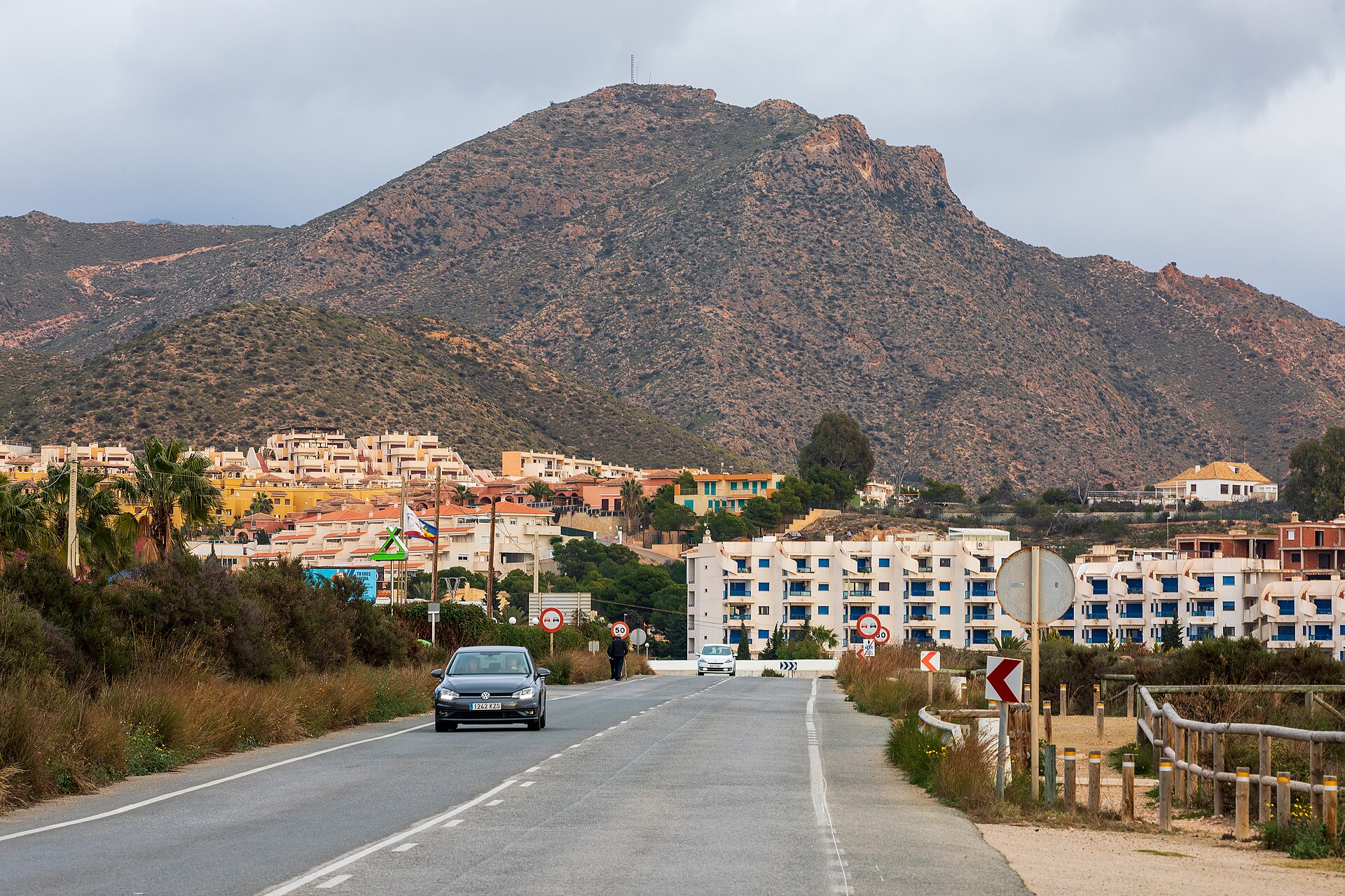 Carretera E-22 hacia El Mojón con el perfil del Cabezo del Horno y urbanización en el borde de la playa, Puerto de Mazarrón.